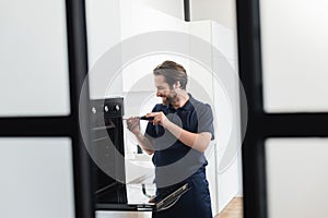 smiling handyman repairing inbuilt electric oven