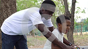 Smiling Happy African American father helps his son learn cycling on bicycle in park.
