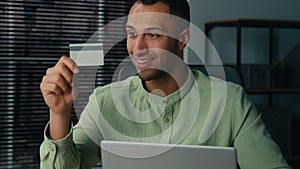 Smiling happy african american man male businessman client customer pay remote credit card enter data in laptop indoors