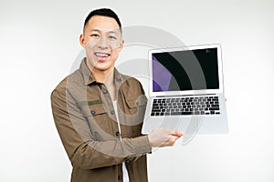 Smiling happy asian man holding laptop with mockup in his hands on a white studio background