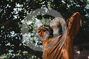 Smiling and happy Asian woman wearing an orange raincoat outdoors in the rain