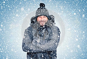 Smiling happy bearded man in winter clothes warms his hands, cold, snow, frost, blizzard