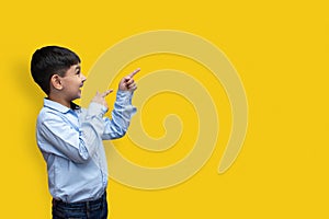 Smiling happy boy pointing finger away at copy space isolated over plain background