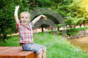 Smiling happy boy sitting on bench near lake. Summer time weekend mood.