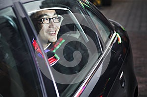 Smiling and happy businessman looking through car window at the night