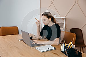 Businesswoman in headphones sits at desk, looks at laptop screen, making notes, participating in self-improvement webinar, having
