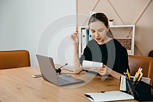 Businesswoman in headphones sits at desk, looks at laptop screen, making notes, participating in self-improvement webinar, having