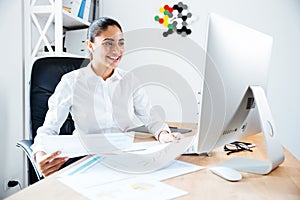 Smiling happy businesswoman holding reports and looking at computer