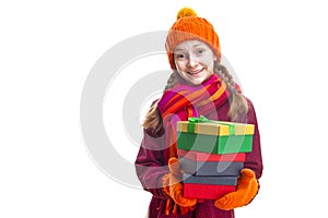 Smiling Happy Caucasian Little Girl In Orange Beanie, Scarf and Mittens With Pile of Colorful Giftboxes.