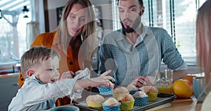 Smiling happy Caucasian parents celebrate son`s birthday, he takes a muffin from tray. Togetherness concept slow motion.