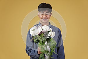 Smiling happy cheerful young asian man dressed casually holding flower bouquet isolated on yellow background