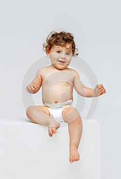 Vertical portrait of little cute toddler boy, baby in diaper joyfully sitting and laughing isolated over white studio