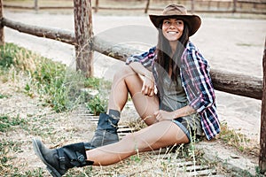 Smiling happy cowgirl sitting and resting at the ranch fence