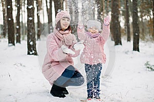 Smiling happy cute child daughter throwing snow up and having fun on a walk with her pretty loving mother. Mom and child