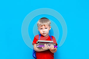 Smiling happy cute clever boy with backpack. Child with a pile of books in his hands. blue background. Ready for school. Back to