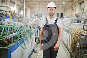 Smiling and happy employee. Industrial worker indoors in factory. Young technician with hard hat