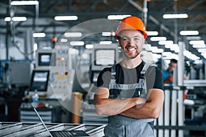 Smiling and happy employee. Industrial worker indoors in factory. Young technician with orange hard hat