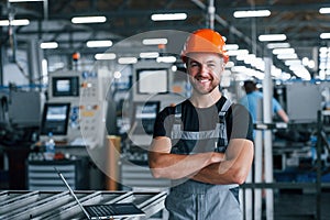 Smiling and happy employee. Industrial worker indoors in factory. Young technician with orange hard hat