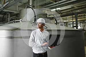 Smiling and happy employee. Industrial worker indoors in factory. Young technician with white hard hat