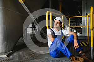 Smiling and happy employee. Industrial worker indoors in factory. Young technician with white hard hat