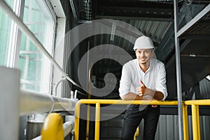Smiling and happy employee. Industrial worker indoors in factory. Young technician with white hard hat
