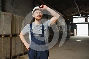 Smiling and happy employee. Industrial worker indoors in factory. Young technician with white hard hat.