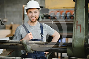 Smiling and happy employee. Industrial worker indoors in factory. Young technician with white hard hat.