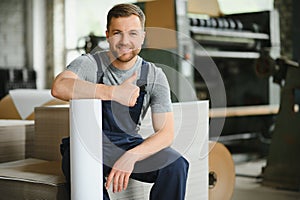 Smiling and happy employee. Industrial worker indoors in factory. Young technician with white hard hat.