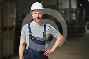 Smiling and happy employee. Industrial worker indoors in factory. Young technician with white hard hat.