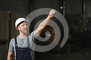 Smiling and happy employee. Industrial worker indoors in factory. Young technician with white hard hat.