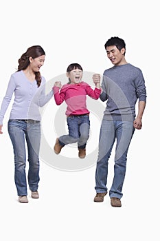 Smiling and happy family enjoying themselves and swinging their daughter in mid-air, studio shot