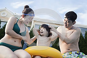 Smiling happy family helping son put on goggles by the poolside