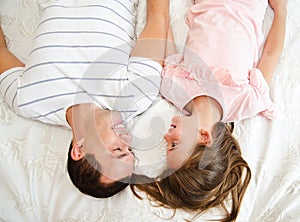 Smiling happy father with his little daughter child lying on the bed and having fun
