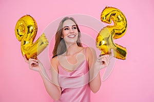 Smiling happy girl holds gold foil balloon isolated on pink background. BIRTHDAY PARTY concept