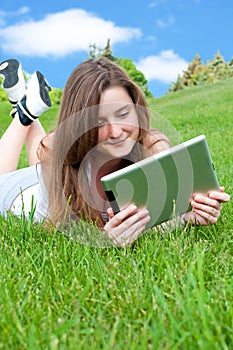 Smiling happy girl lying on grass with tablet.