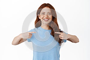 Smiling happy girl with red hair pointing at herself, pick me, want to volunteer, self-promoting her personal skills