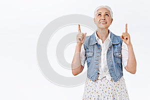 Smiling happy, good-looking senior woman grinning amused, raise head and pointing up contemplate something astonishing