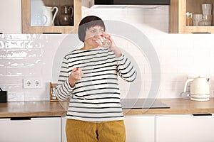 Smiling happy healthy senior woman at home holding glass of natural water taking daily pill for good health and senile