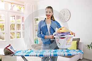 Smiling and happy housewife posing with iron and basket with clean laundry