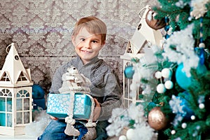 Smiling happy little boy sitting with christmas present near the chrismas tree