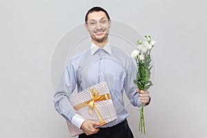 Smiling happy man with present box and bouquet of flowers, congratulate her girlfriend with birthday