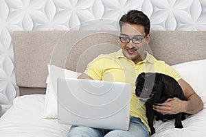 Smiling happy man sitting on the bed and hugging his lovely pet