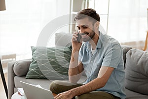 Smiling happy man using laptop and talking on phone at home