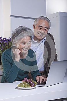 Smiling happy mature couple looking at laptop in the kitchen