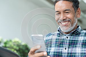 Smiling happy mature man with white stylish short beard using smartphone gadget serving internet