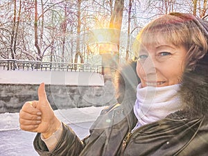 Smiling happy mature middle aged Woman taking selfie and Giving Thumbs Up in Front of fence of park in tour in city on a