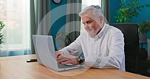 Smiling happy middle aged 50s old senior man using laptop computer technology working online, surfing