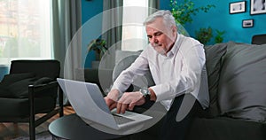 Smiling happy middle aged 50s old senior man using laptop computer technology working online, surfing