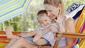 Smiling and happy mother hugging and cuddling her baby son, child have fun playing together sitting on deck chair, in the home