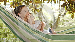 Smiling happy mother hugs and cuddle her little baby son, relaxing  lying together in the hammock. Child plays with pacifier, in